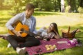 Loving man playing guitar and singing serenade to his girlfriend on romantic picnic in park Royalty Free Stock Photo