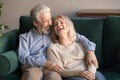 Loving middle aged husband embracing laughing wife, sitting on couch