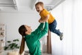 Loving mom lifting her little son in air while spending time together at home, holding kid in hands and smiling Royalty Free Stock Photo