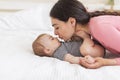 Loving mommy kissing her baby, enjoying time with her infant daughter, lying on bed at home, side view Royalty Free Stock Photo