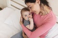 Loving mother cuddling and resting with her infant daughter on bed, mom holding cute newborn baby on hands Royalty Free Stock Photo