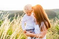 Loving mother holding her son in her arms while standing in a picturesque field at sunset.