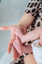 Loving mother holding tiny feet of newborn in hand near houseplant at home on sunny day. Maternity, motherhood concept. Royalty Free Stock Photo