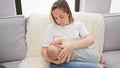 Loving mother at home, sitting on the fond family room sofa, breastfeeding her baby, relishing this intimate moment of motherhood, Royalty Free Stock Photo