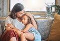 Loving mother kissing her daughter on the forehead as she falls asleep in her arms while sitting on the couch at home Royalty Free Stock Photo