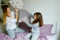 Loving mother and school kid girl making pillow fight together. Happy family, woman and cute daughter having fun Royalty Free Stock Photo