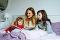 Loving mother and two little girls reading book together. Happy family, woman and cute daughters, toddler sister and Royalty Free Stock Photo