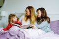 Loving mother and two little girls reading book together. Happy family, woman and cute daughters, toddler sister and Royalty Free Stock Photo