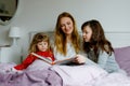 Loving mother and two little girls reading book together. Happy family, woman and cute daughters, toddler sister and Royalty Free Stock Photo