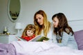 Loving mother and two little girls reading book together. Happy family, woman and cute daughters, toddler sister and Royalty Free Stock Photo