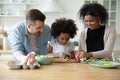 Loving multiethnic parents teach biracial small daughter cooking in kitchen