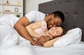 Multiracial couple cuddling in bed at home, hugging each other, having intimate foreplay after waking up in morning Royalty Free Stock Photo