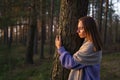 Loving nature concept: relaxed woman hugging tree trunk in autumn forest with closed eyes at sunset Royalty Free Stock Photo