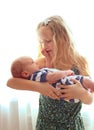 Loving older sister blonde sweetheart touching and gentle holds her newborn brother in her arms, cute tiny baby. Royalty Free Stock Photo