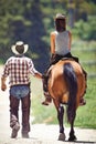 Loving the outdoors. Rear view of a cowboy leading a young woman on a horse along a country lane.