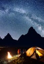 Loving pair - guy and girl sitting face to face in front tent near bonfire under shines starry sky at night