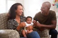 Loving Parents Sitting In Chair Cuddling Baby Son In Nursery At Home