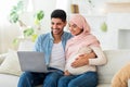 Loving pregnant muslim couple choosing furniture for baby room online, using laptop on sofa in living room, empty space Royalty Free Stock Photo