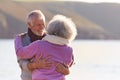 Loving Retired Couple Hugging Standing By Shore On Winter Beach Vacation Against Flaring Sun Royalty Free Stock Photo