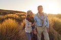 Loving Retired Couple Walking Arm In Arm Through Sand Dunes On Beach Vacation Against Flaring Sun Royalty Free Stock Photo