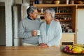 Loving retired elderly biracial couple laughing at each other while standing in modern kitchen. Royalty Free Stock Photo