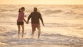 Loving Retired Senior Couple On Vacation Walking Along Beach Through Waves Holding Hands At Sunrise Royalty Free Stock Photo