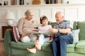 Grandparents reading book with little granddaughter on sofa in living room