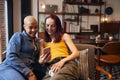 Loving Same Sex Female Couple Sitting On Sofa At Home Looking At Mobile Phone Together