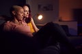 Loving Same Sex Female Couple Sitting On Sofa At Home Watching Evening TV And Relaxing Together