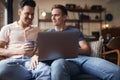 Loving Same Sex Male Couple Sitting On Sofa Using Laptop As They Relax At Home Together Royalty Free Stock Photo