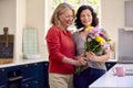 Loving Same Sex Mature Female Couple In Kitchen With Woman Giving Partner Flowers Royalty Free Stock Photo