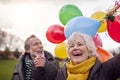 Loving Senior Couple Holding Balloons Enjoying Autumn Or Winter Walk Through Park Together Royalty Free Stock Photo