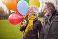 Loving Senior Couple Holding Balloons Enjoying Autumn Or Winter Walk Through Park Together Royalty Free Stock Photo