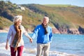 Loving Senior Couple Holding Hands As They Walk Along Shoreline Of Beach By Waves Royalty Free Stock Photo