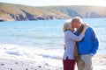 Loving Senior Couple Hugging As They Walk Along Shoreline Of Beach By Waves Royalty Free Stock Photo