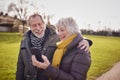 Loving Senior Couple Looking At Mobile Phone Enjoying Autumn Or Winter Walk Through Park Together Royalty Free Stock Photo