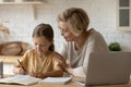 Friendly aged woman teacher watching girl pupil writing maths task