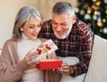 Loving senior man husband giving Christmas present gift box to happy surprised wife