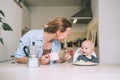 Loving smiling mother and baby eating breakfast and have fun in kitchen at home. Beautiful mother enjoys her life on maternity Royalty Free Stock Photo