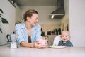 Loving smiling mother and baby eating breakfast and have fun in kitchen at home. Beautiful mother enjoys her life on maternity Royalty Free Stock Photo
