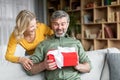 Loving wife surprising her middle aged husband with gift at home