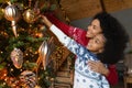 Happy biracial mom and small daughter decorate fir-tree Royalty Free Stock Photo