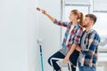 Couple in casual plaid shirts paint house wall together. DIY renovation concept. Royalty Free Stock Photo