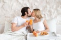 Loving young couple having breakfast in bed together, kissing, spending honeymoon at hotel Royalty Free Stock Photo