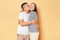 Loving young couple wife and husband wearing casual attires standing isolated over beige background hugging each other and man