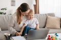 Loving young mom playing with son while working on laptop, sitting on sofa and tickling child, enjoying maternity leave Royalty Free Stock Photo