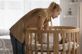 Loving young mother putting sleeping baby in wooden crib