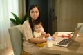 Loving young mother working remotely on laptop while taking care of her baby Royalty Free Stock Photo