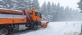 Low-agle of snow ploughing truck cleaning the road after heavy snowfall snowy forest background Royalty Free Stock Photo