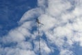 Low angle of an antenna with wires against the blue sky and floating clouds on a bright day Royalty Free Stock Photo
